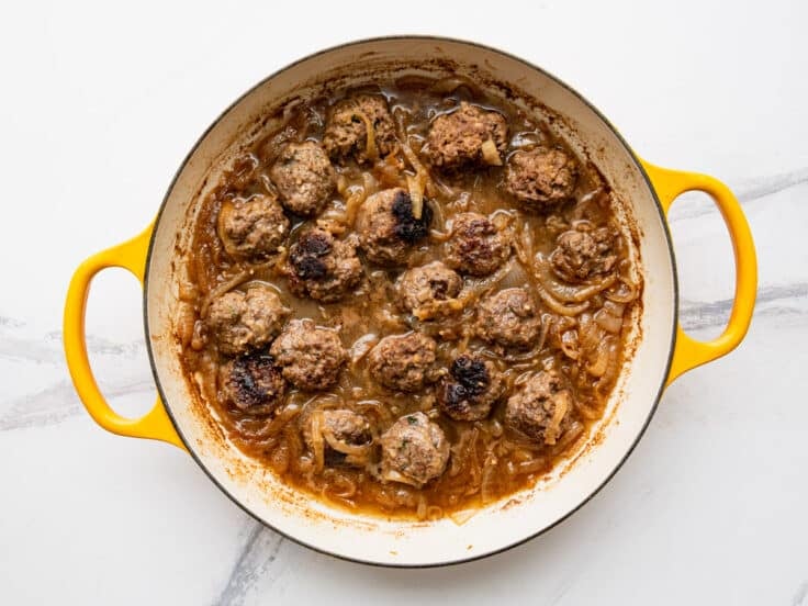 Simmering French onion meatballs with caramelized onions and broth.