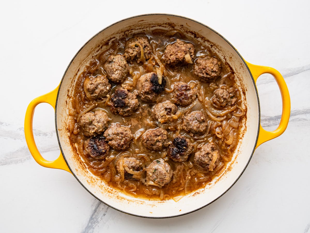 Simmering French onion meatballs with caramelized onions and broth.