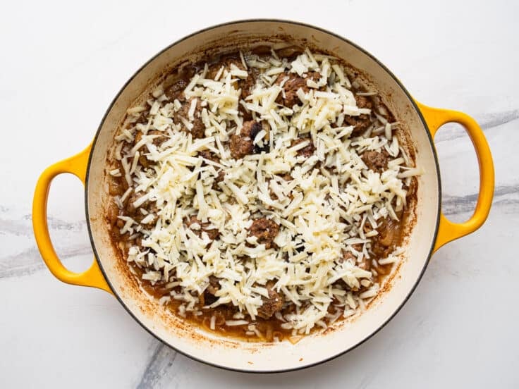 Sprinkling grated Gruyere over French onion meatballs.