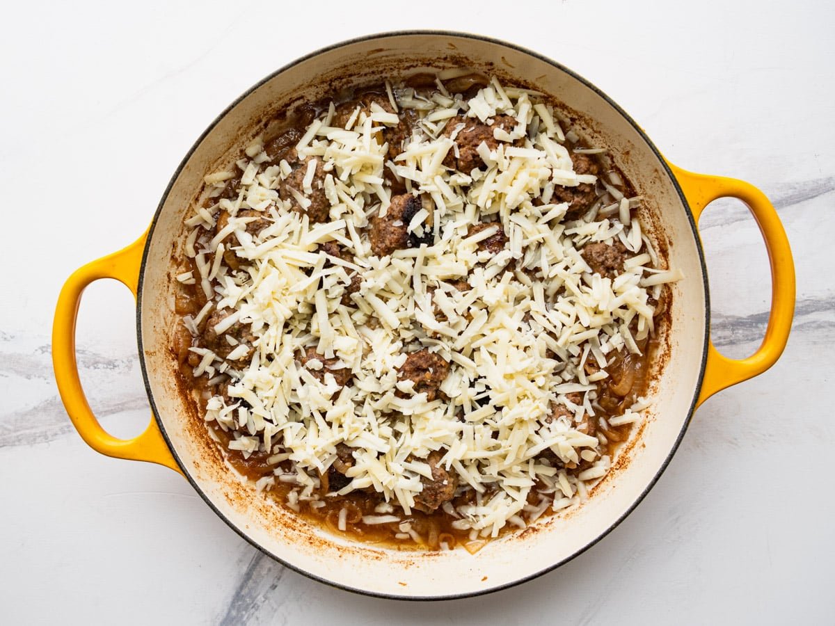 Sprinkling grated Gruyere over French onion meatballs.