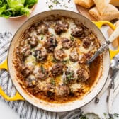 Horizontal overhead shot of French onion soup meatballs in a skillet with melted Gruyere cheese on top.
