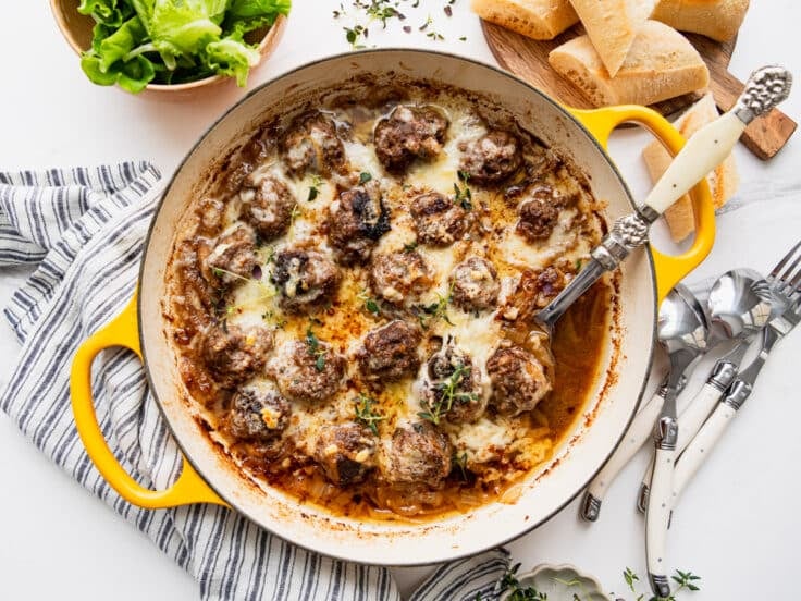 Horizontal overhead shot of French onion soup meatballs in a skillet with melted Gruyere cheese on top.