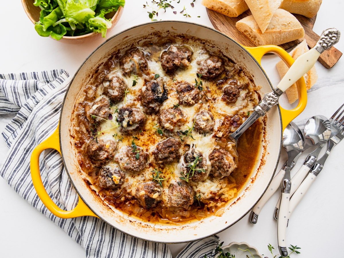 Horizontal overhead shot of French onion soup meatballs in a skillet with melted Gruyere cheese on top.