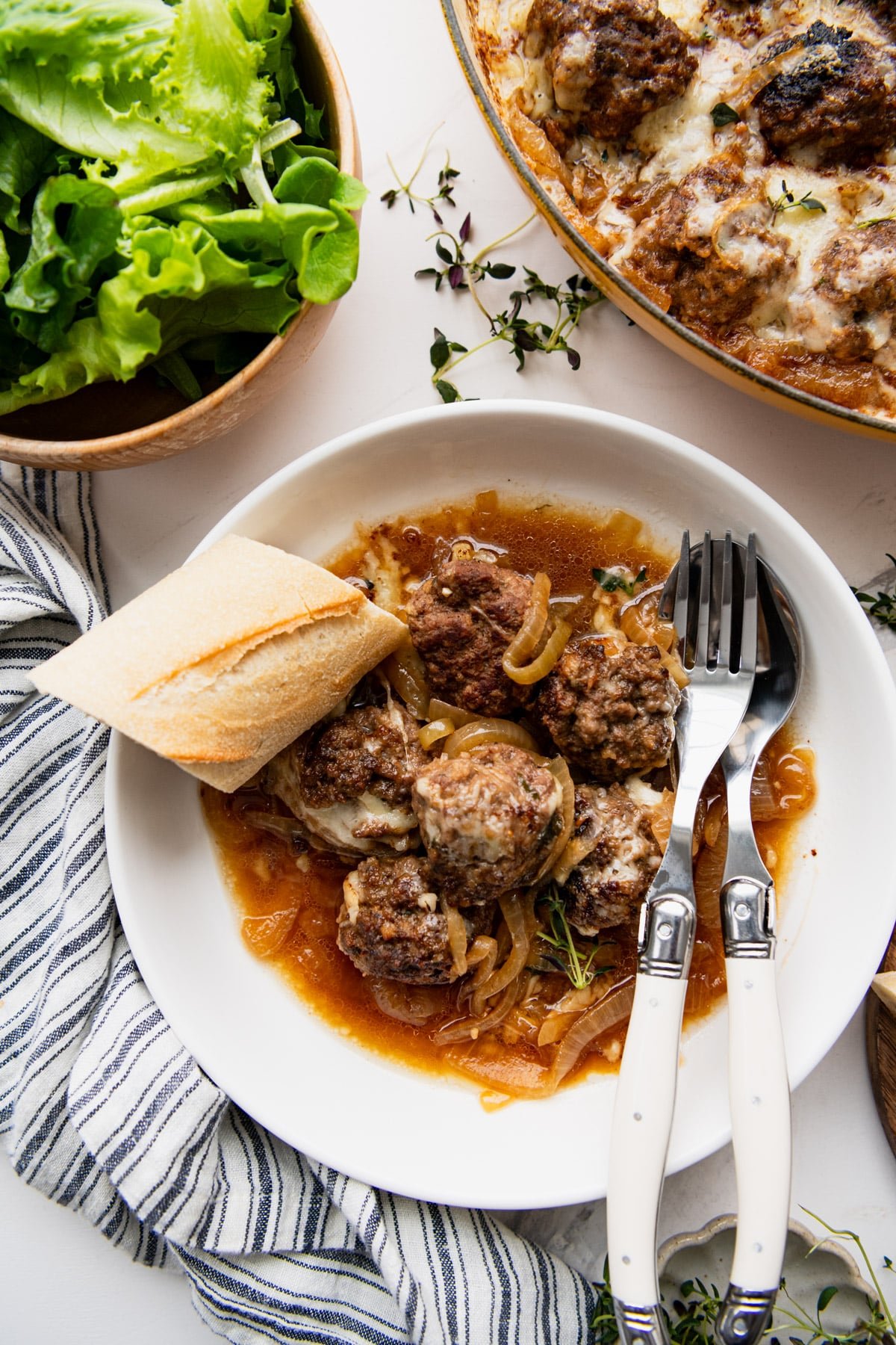 Baguette served with a bowl of French onion meatballs and a side salad.