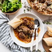 Horizontal overhead image of French onion meatballs in a white bowl with a baguette.