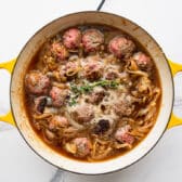 Adding broth, onions, and herbs to the skillet with the meatballs.