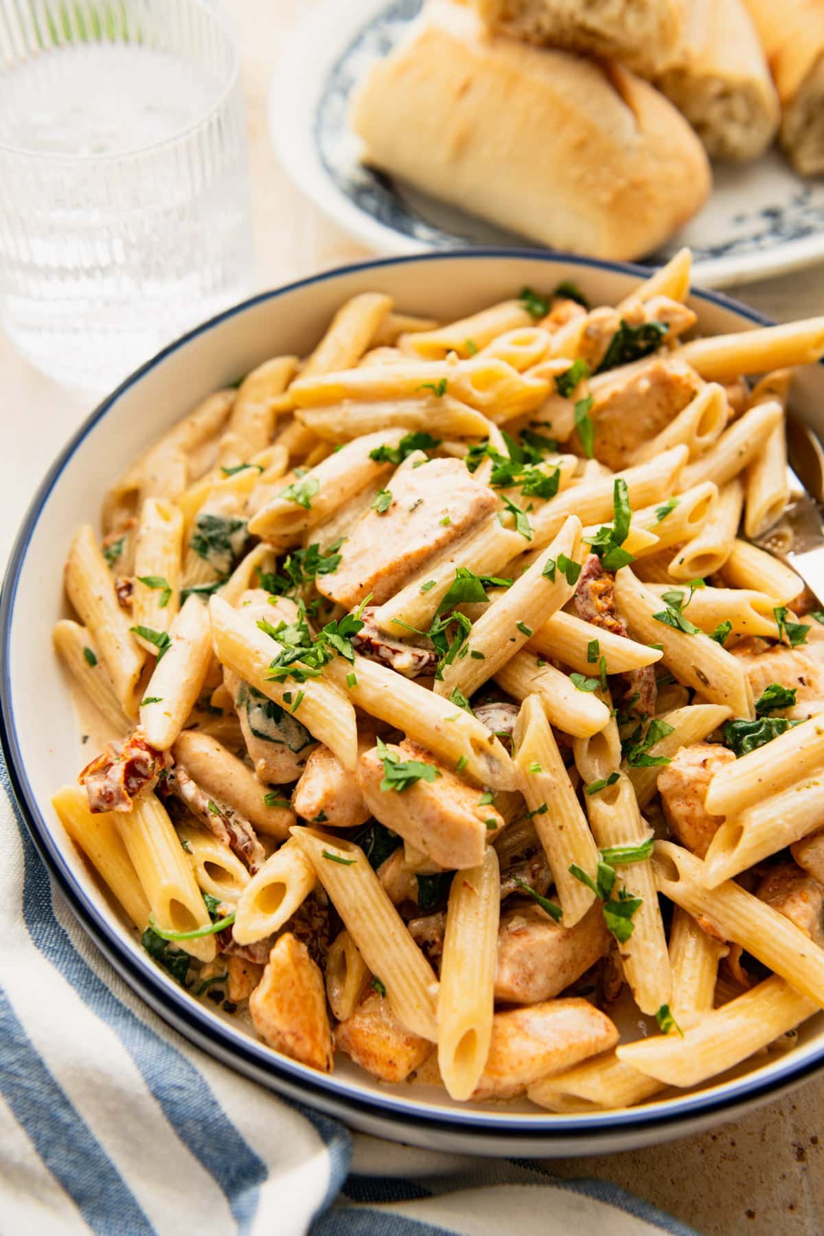 A bowl of creamy Tuscan chicken pasta with a side of baguette.