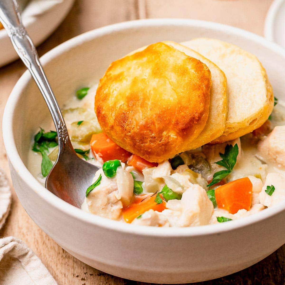 Close up square image of a bowl of crock pot chicken pot pie with biscuits.