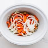 Potatoes and veggies in the bottom of a slow cooker.