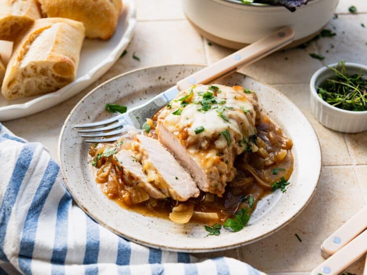 Horizontal side shot of a French onion pork chop on a plate with a side of baguette.