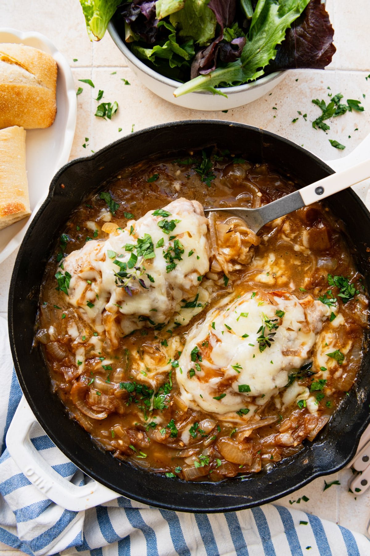 Overhead shot of a serving spoon in a cast iron pan full of French onion pork chops.