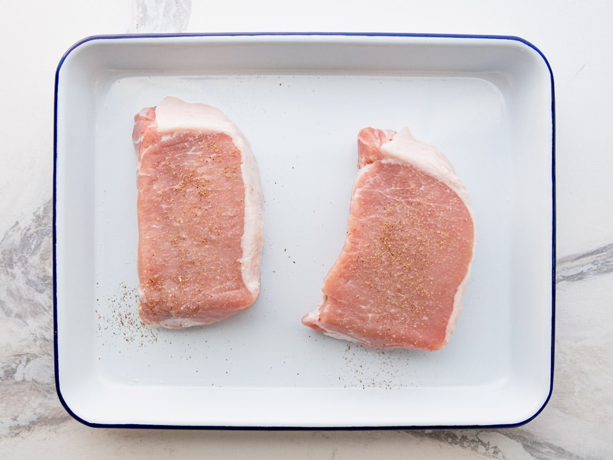 Seasoning pork chops with salt and pepper on a tray.