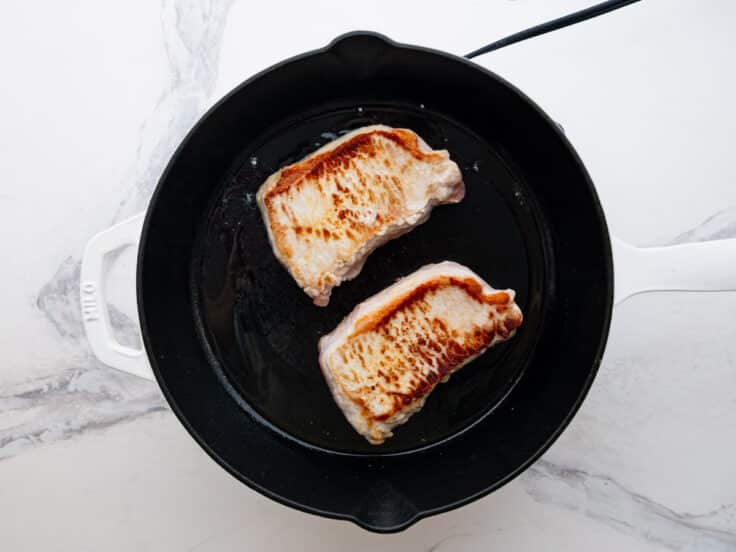 Browning pork chops in a cast iron skillet.