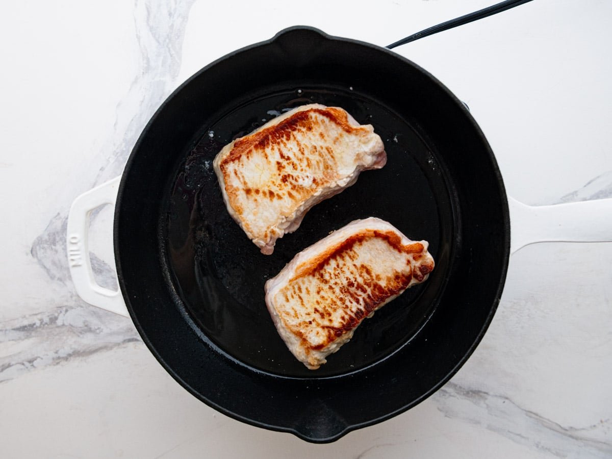 Browning pork chops in a cast iron skillet.