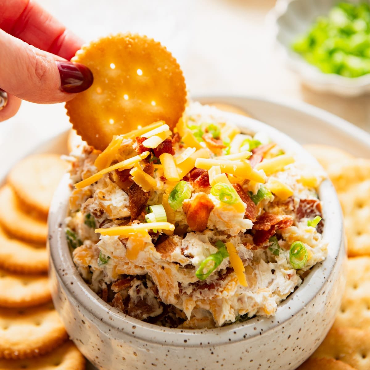 Hand dipping a Ritz cracker in a bowl of Neiman Marcus dip.