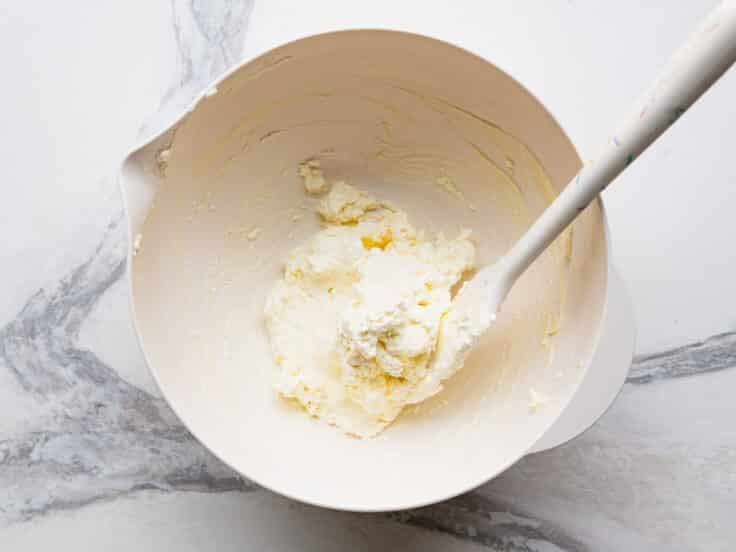 Combining cream cheese and mayo in a white mixing bowl.