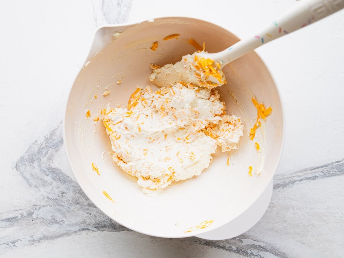 Stirring in grated sharp cheddar cheese.
