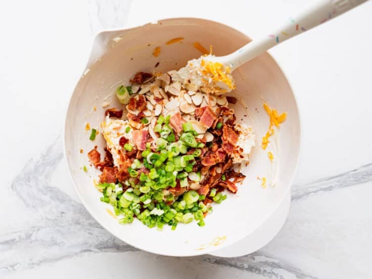 Adding bacon and green onions to the bowl.