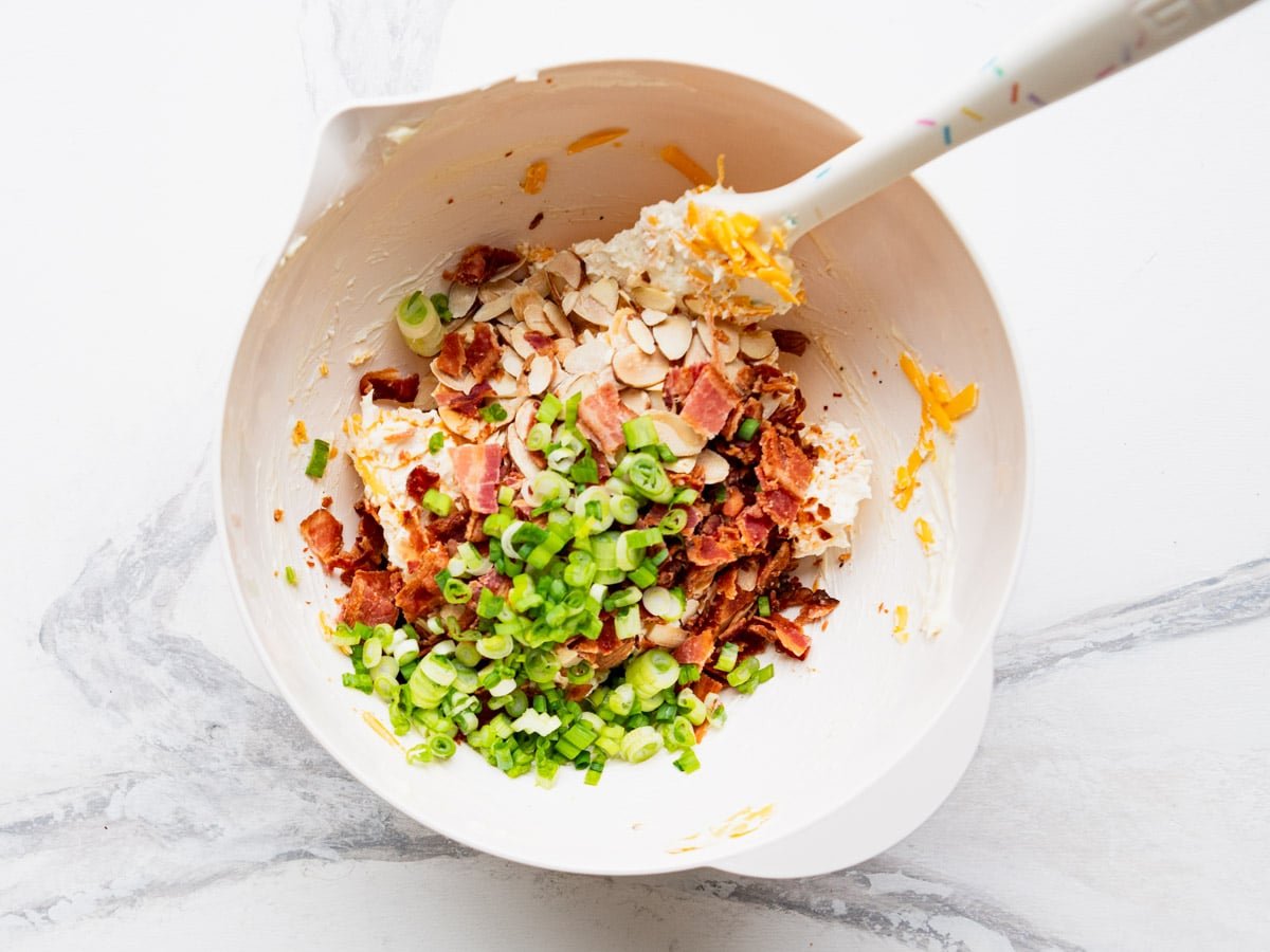 Adding bacon and green onions to the bowl.