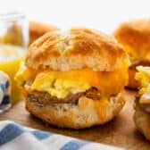 Horizontal side shot of breakfast biscuit sandwiches on a wooden cutting board.