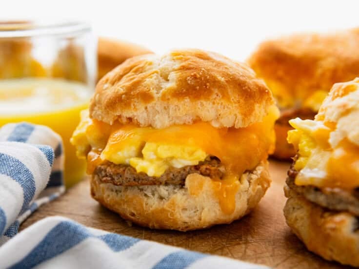 Horizontal side shot of breakfast biscuit sandwiches on a wooden cutting board.