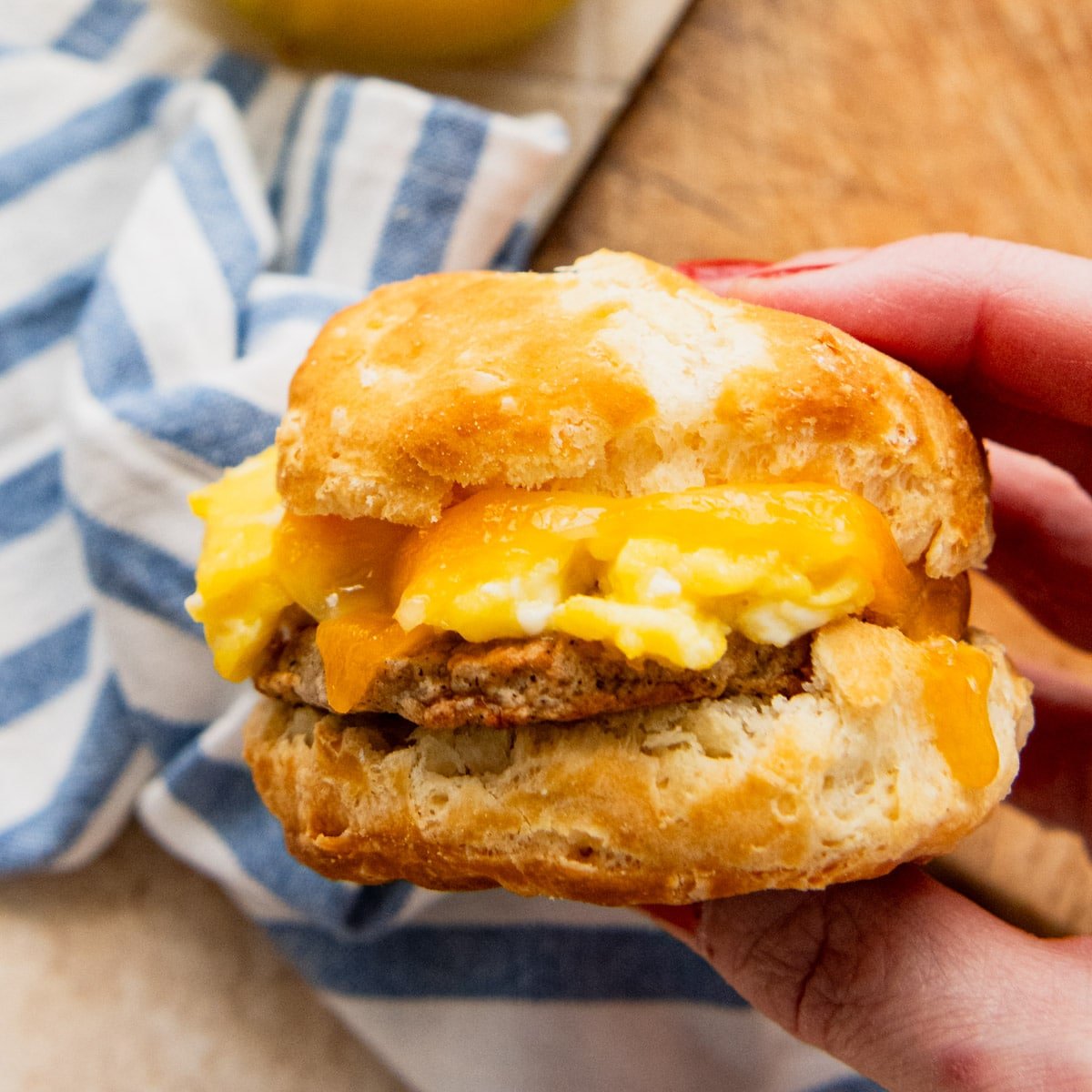 Square side shot of a hand holding a breakfast biscuit sandwich.