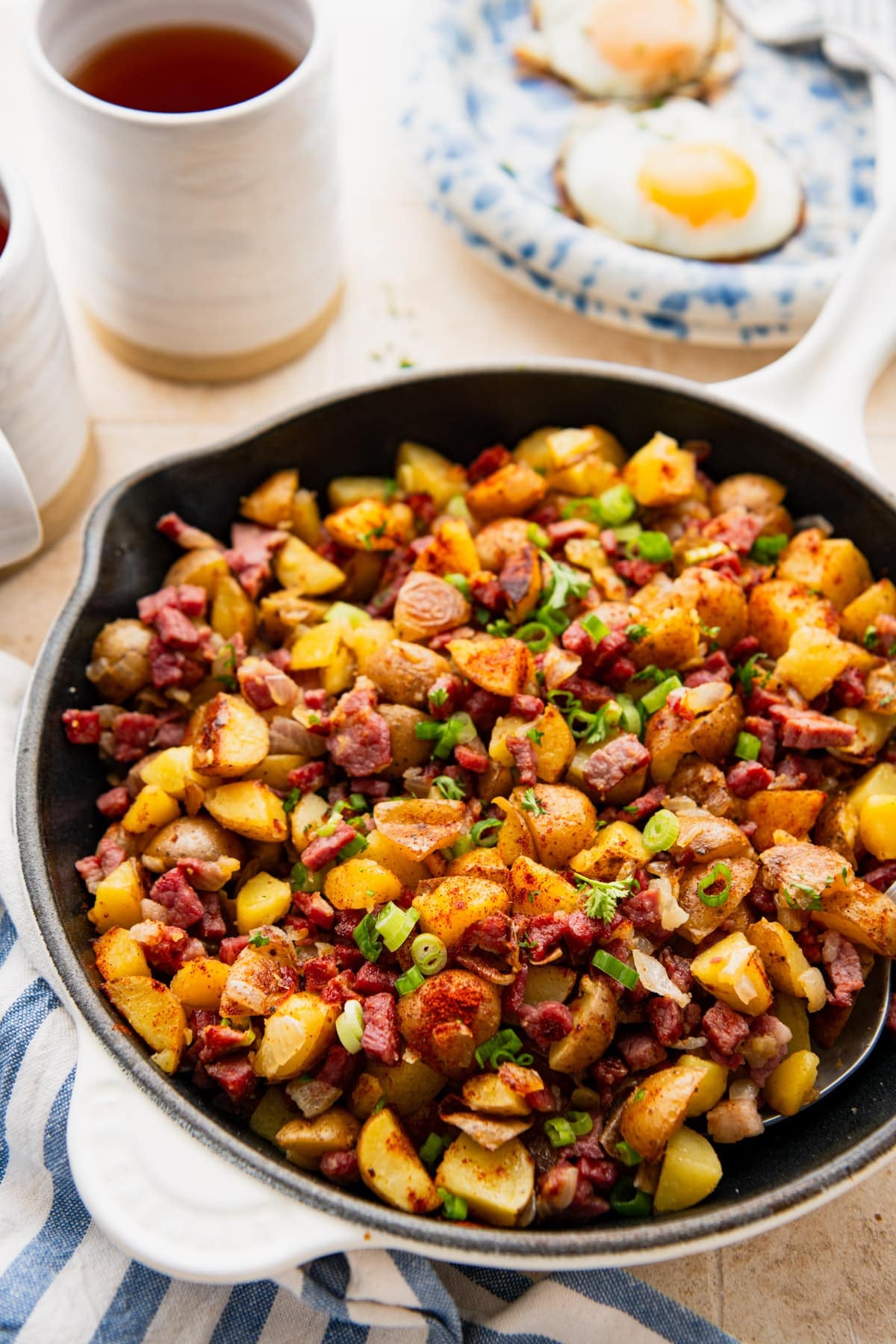 Side shot of a skillet of corned beef hash with fried eggs on a plate in the background.