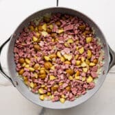 Adding corned beef and potatoes to a skillet.