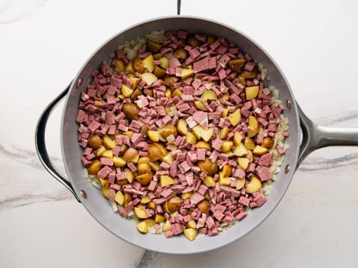 Adding corned beef and potatoes to a skillet.