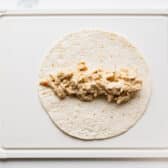 Process shot showing how to assemble cream cheese chicken enchiladas.