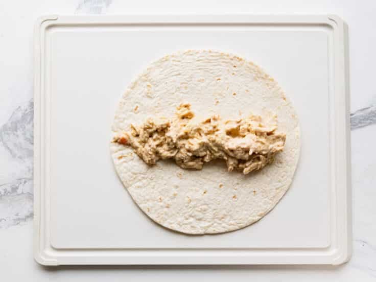 Process shot showing how to assemble cream cheese chicken enchiladas.