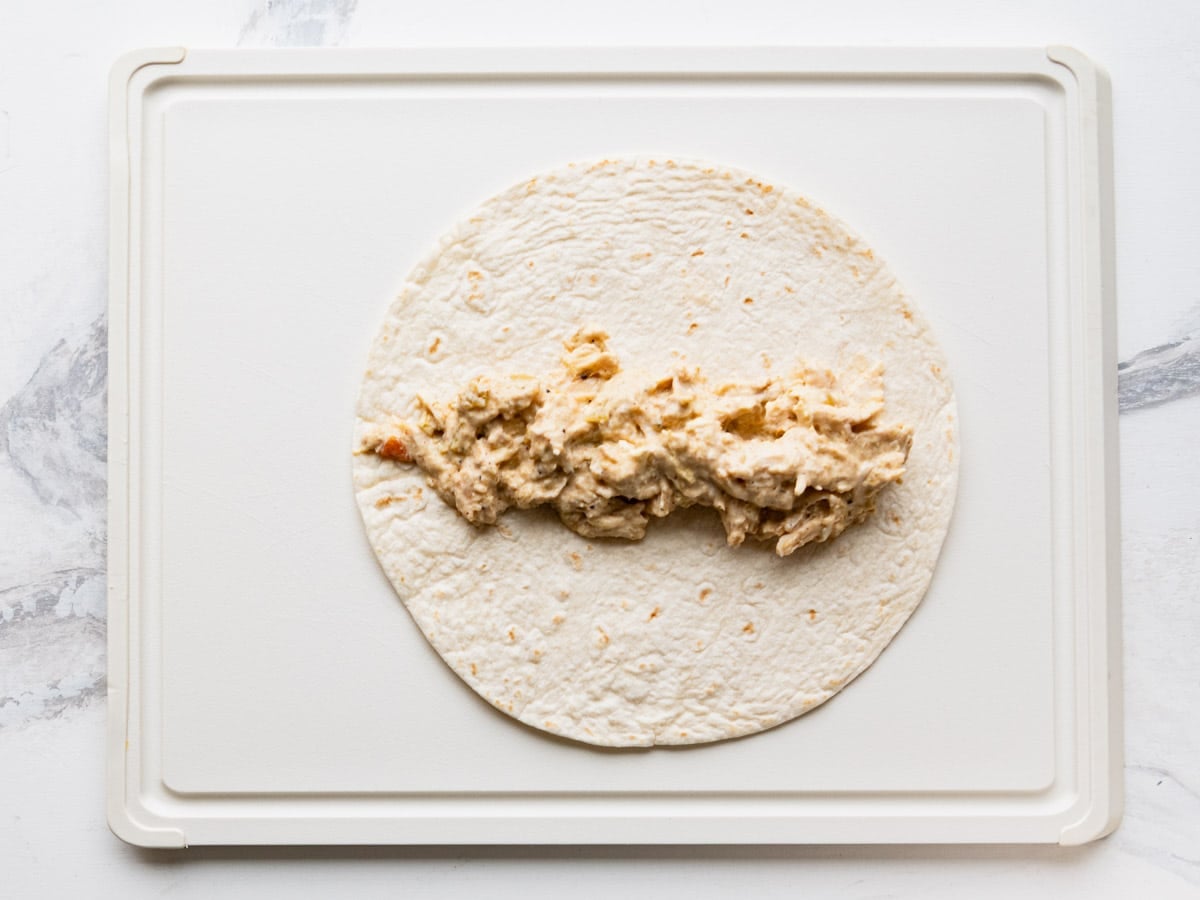 Process shot showing how to assemble cream cheese chicken enchiladas.