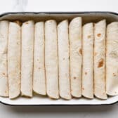 Process shot showing how to arrange chicken enchiladas in a dish.