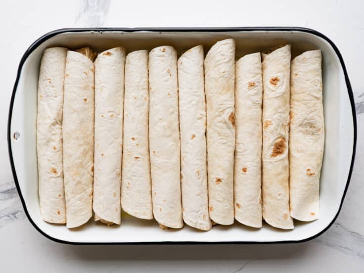 Process shot showing how to arrange chicken enchiladas in a dish.