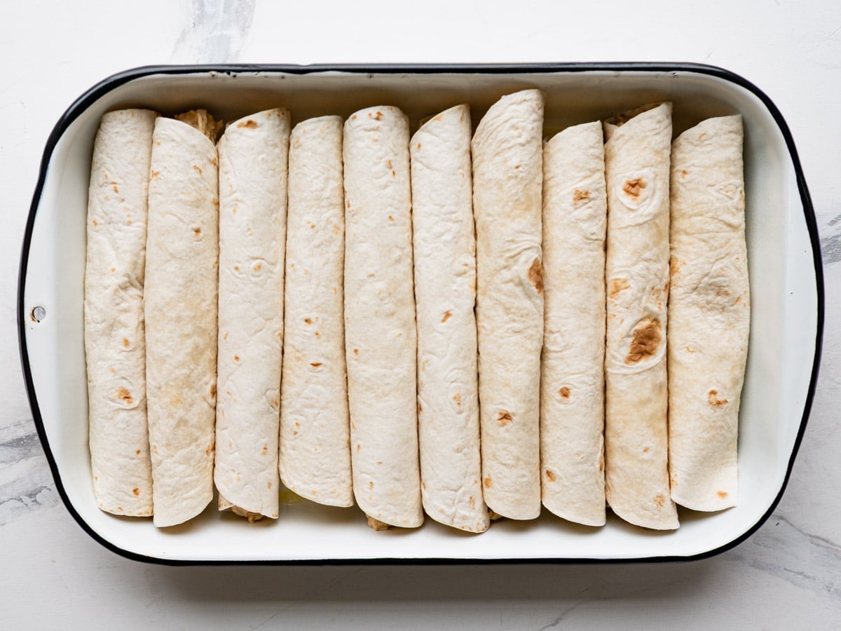 Process shot showing how to arrange chicken enchiladas in a dish.