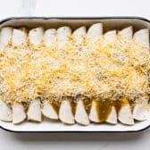 Green enchilada sauce and cheese on top of cream cheese chicken enchiladas.