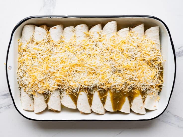 Green enchilada sauce and cheese on top of cream cheese chicken enchiladas.