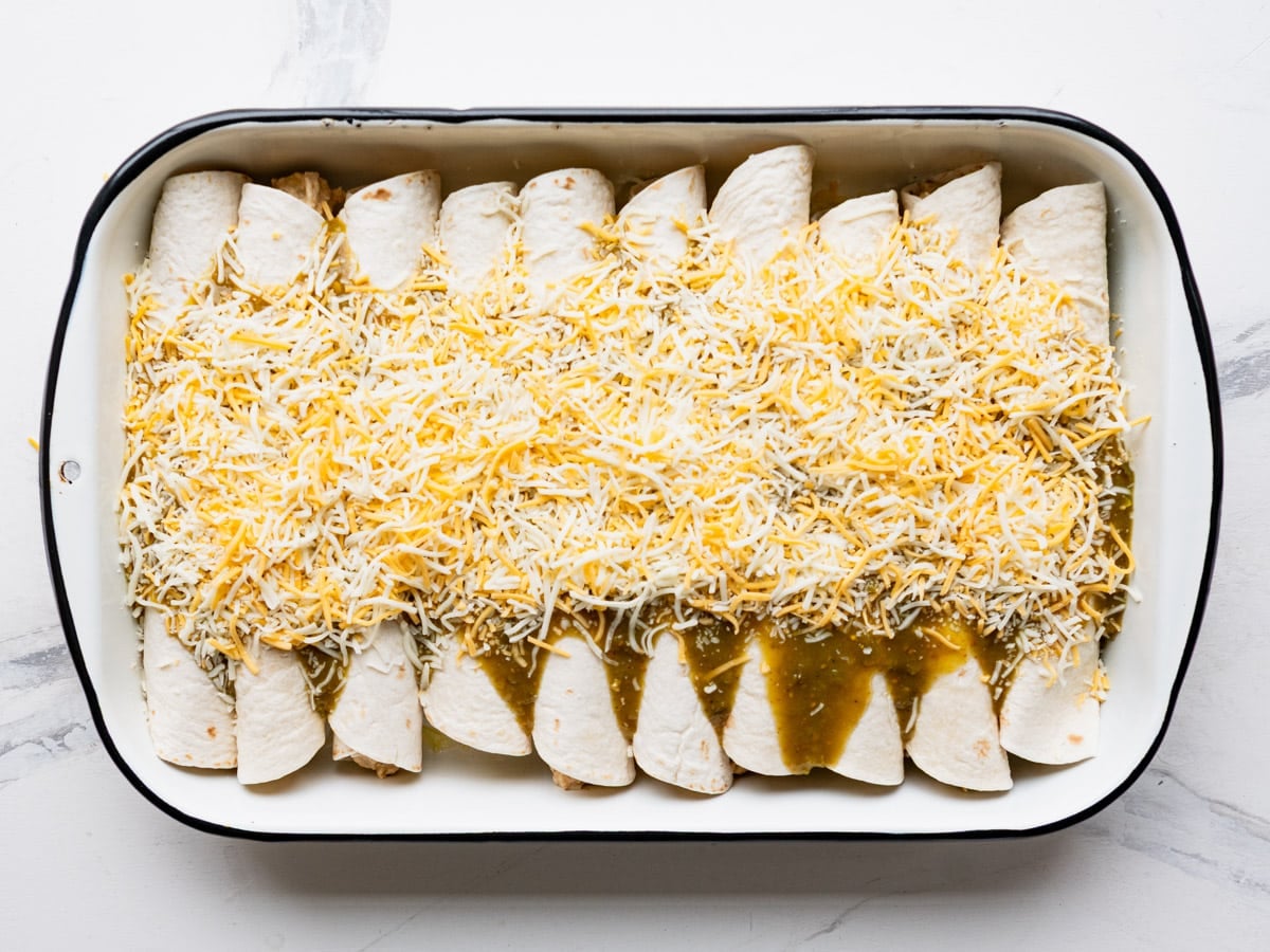 Green enchilada sauce and cheese on top of cream cheese chicken enchiladas.