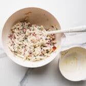 Adding the dressing to bacon ranch pasta salad.