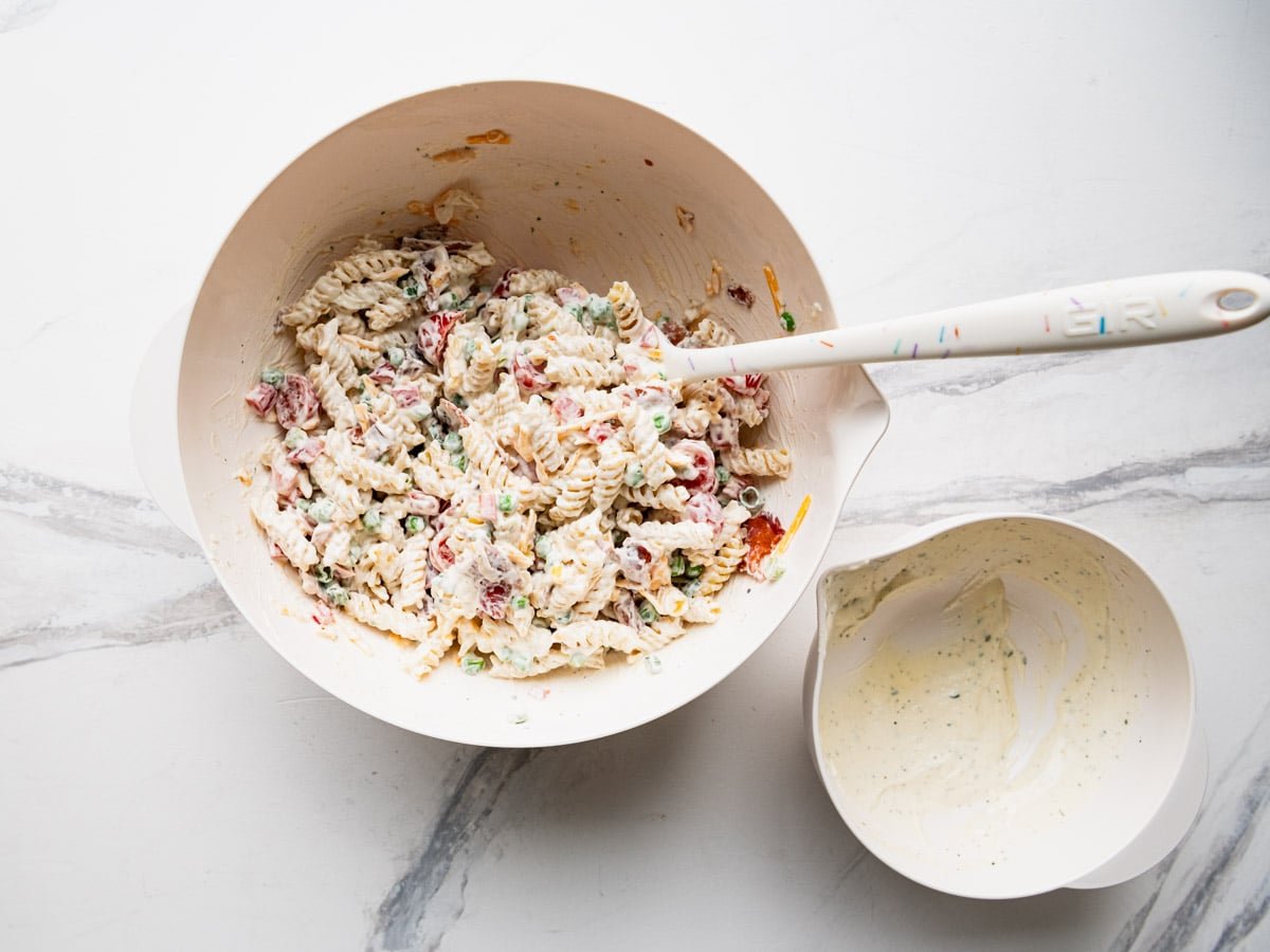 Adding the dressing to bacon ranch pasta salad.