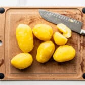 Peeling and dicing boiled potatoes on a cutting board.