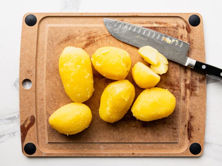 Peeling and dicing boiled potatoes on a cutting board.