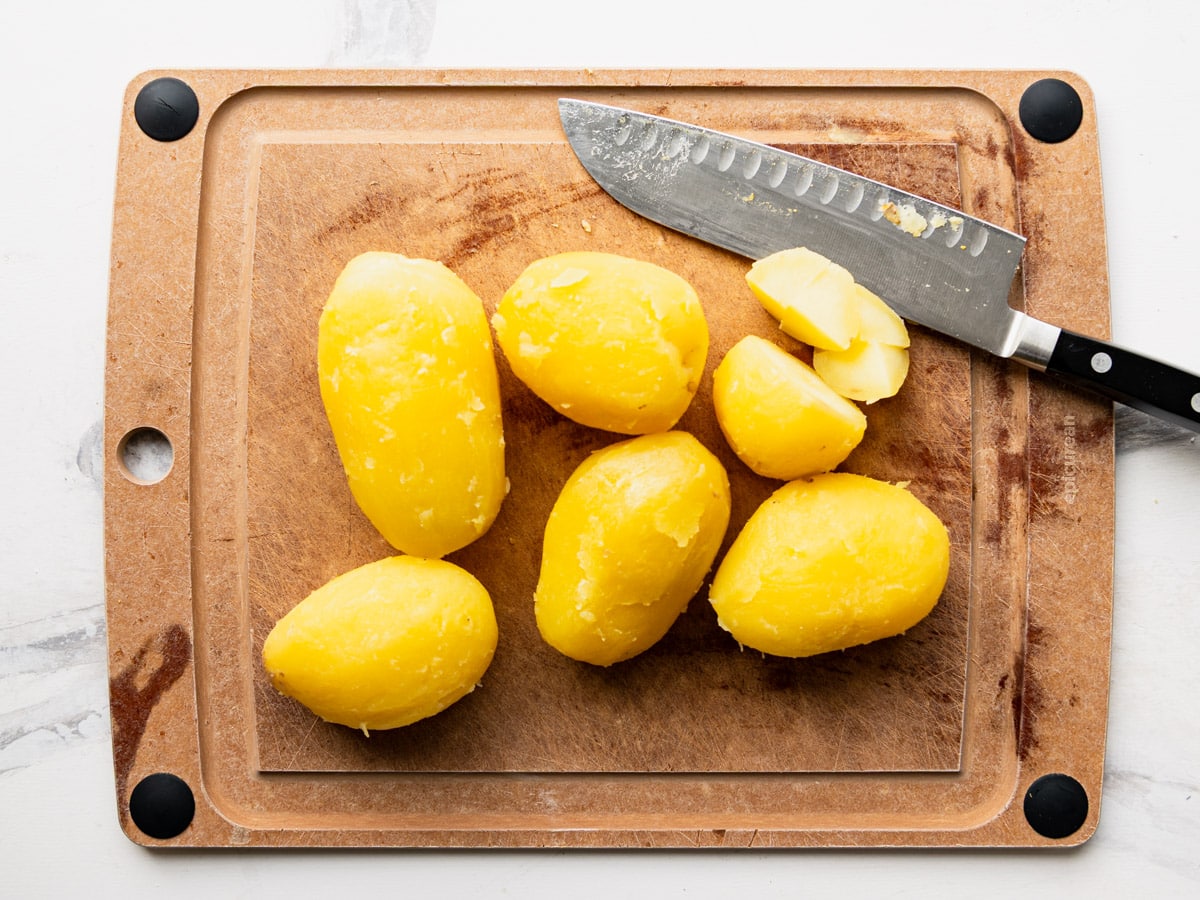 Peeling and dicing boiled potatoes on a cutting board.