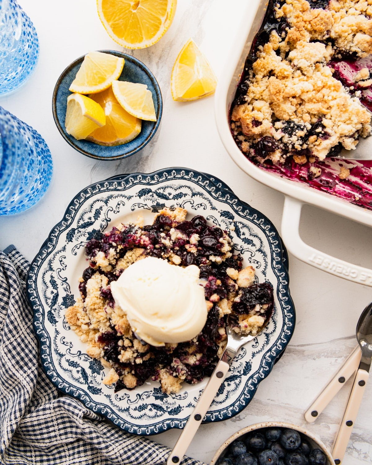 Overhead shot of easy blueberry cobbler with lemons and vanilla ice cream on a white table.