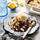 Horizontal side shot of a plate of easy blueberry cobbler with cake mix and a scoop of vanilla ice cream.
