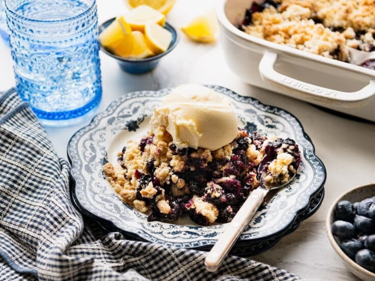 Horizontal side shot of a plate of easy blueberry cobbler with cake mix and a scoop of vanilla ice cream.