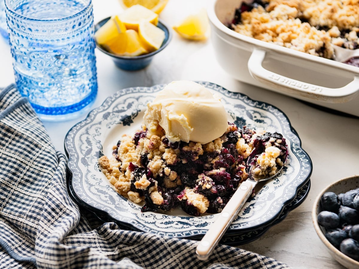 Horizontal side shot of a plate of easy blueberry cobbler with cake mix and a scoop of vanilla ice cream.