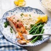 Horizontal side shot of a blue and white dinner plate full of garlic butter salmon, rice, and green beans.