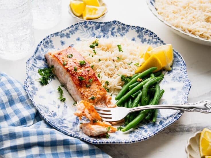 Horizontal side shot of a blue and white dinner plate full of garlic butter salmon, rice, and green beans.
