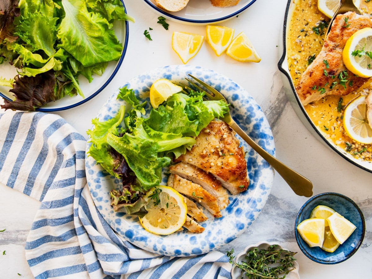 Horizontal overhead shot of a sliced skillet lemon chicken breast on a blue and white plate with a side salad.